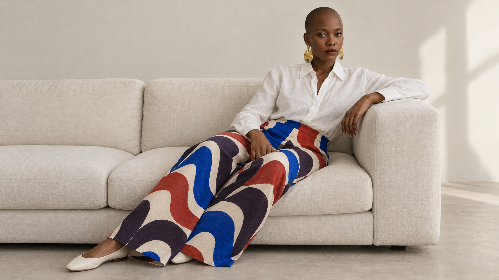 Éditorial NuVoice : chemise blanche et pantalon imprimé, modèle assis sur un canapé blanc